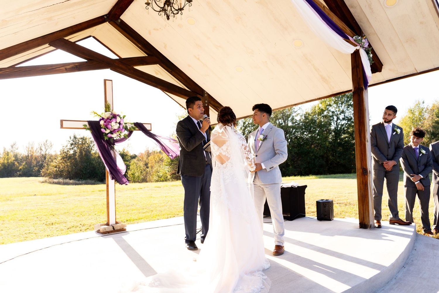 Wedding ceremony setup under white tent canopy with wooden beams and natural lighting.