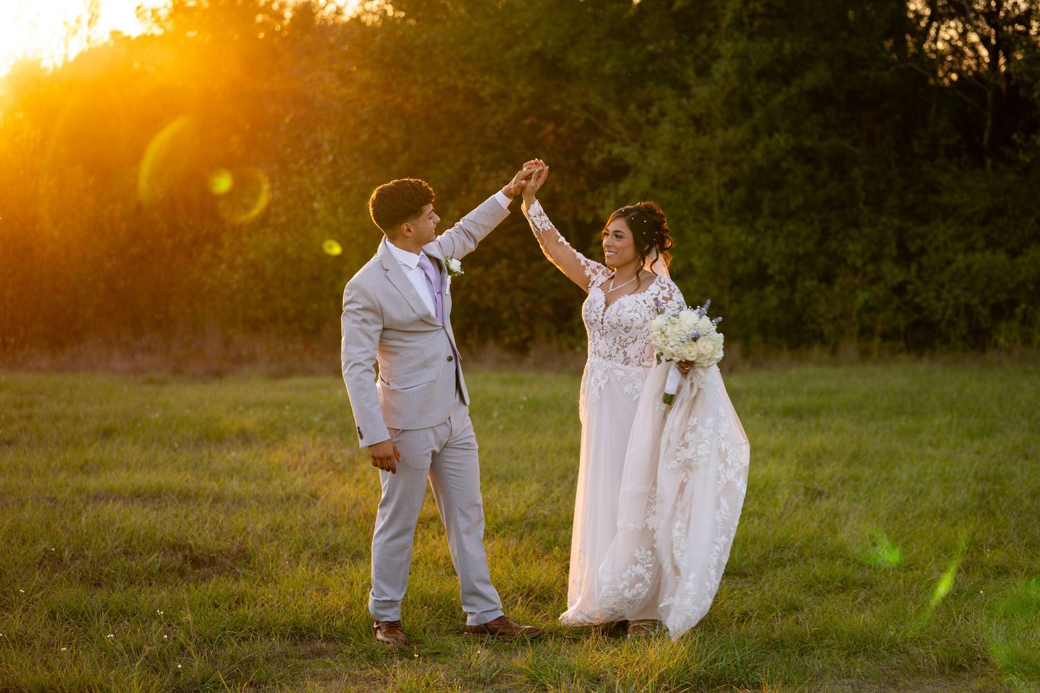Newlyweds share romantic dance moves during golden hour wedding photos in field.