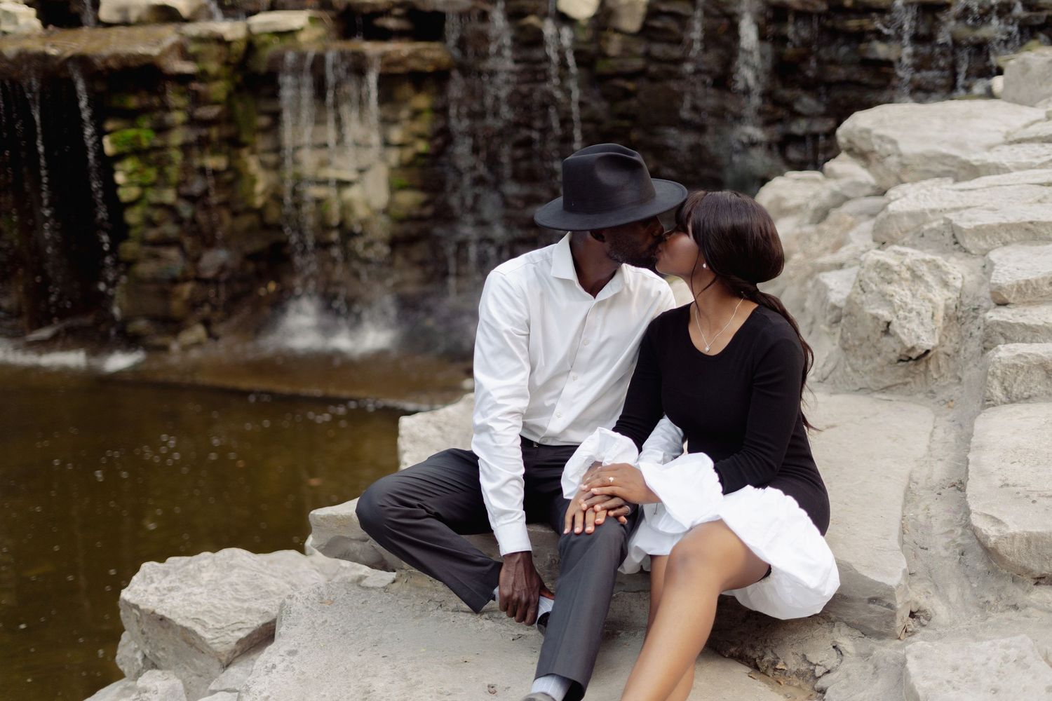 Couple relaxing by waterfall on rocky terrain.