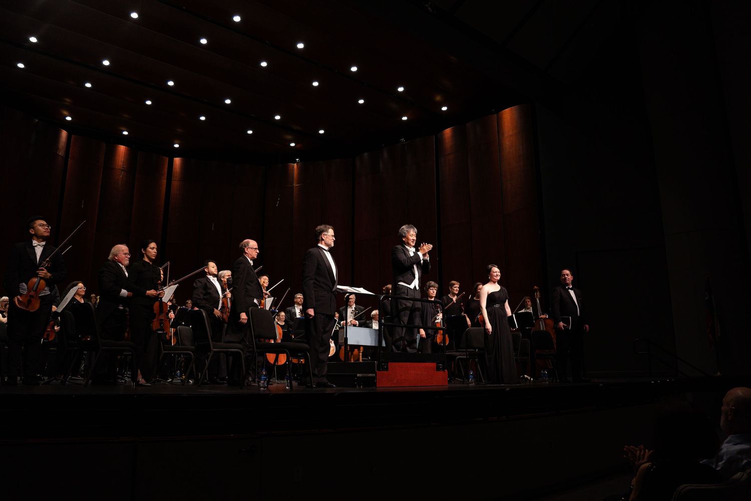 Wide shot of performers lined up on dark stage with minimal lighting.