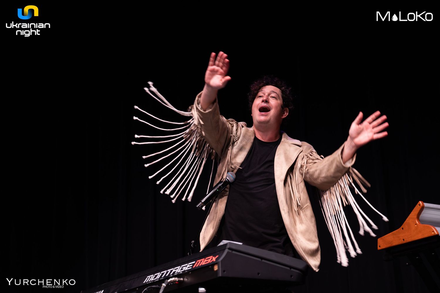 Performer in fringed jacket playing keyboard with dramatic gesture.