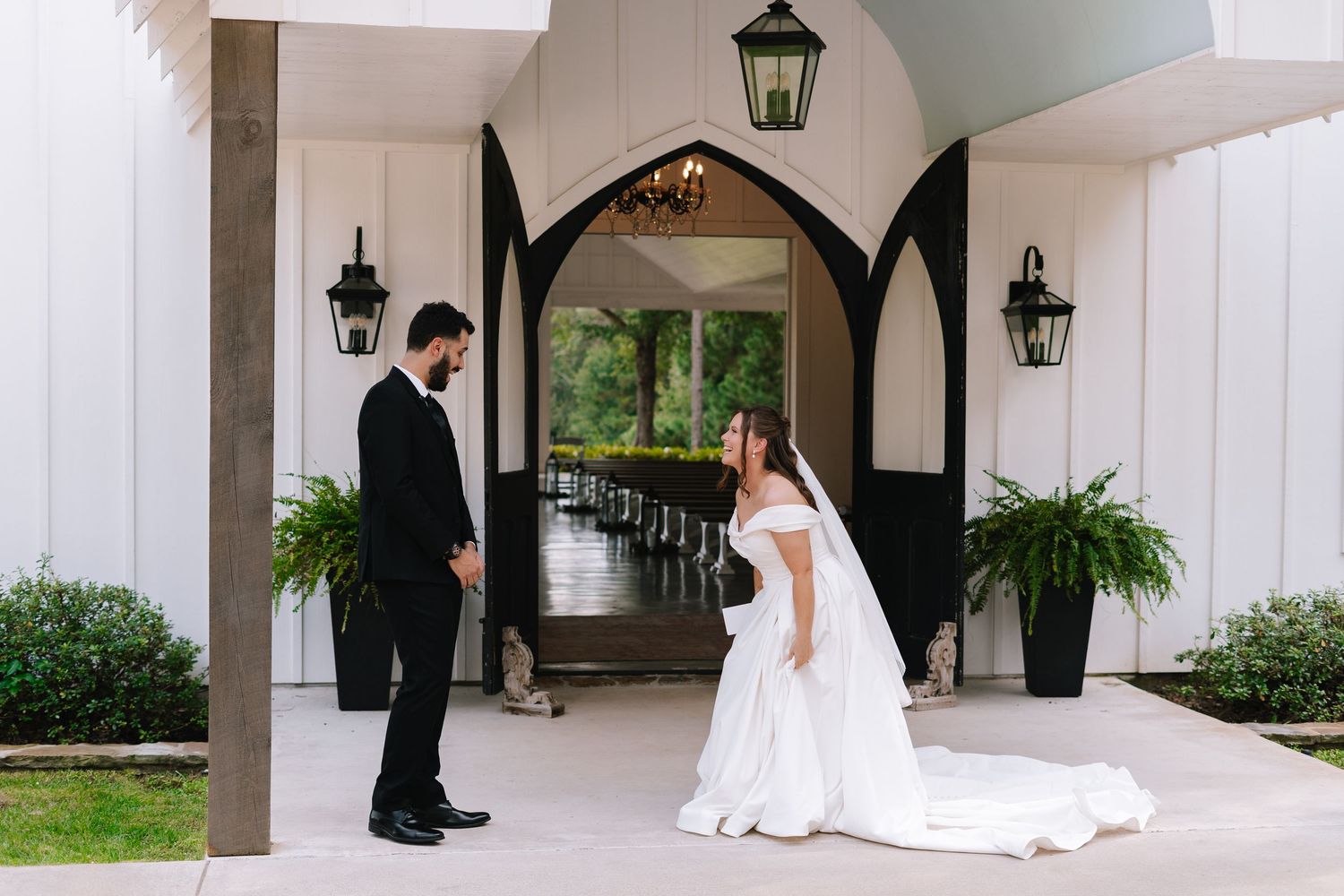 A couple shares their first look moment in front of an elegant white chapel entrance with gothic arches.