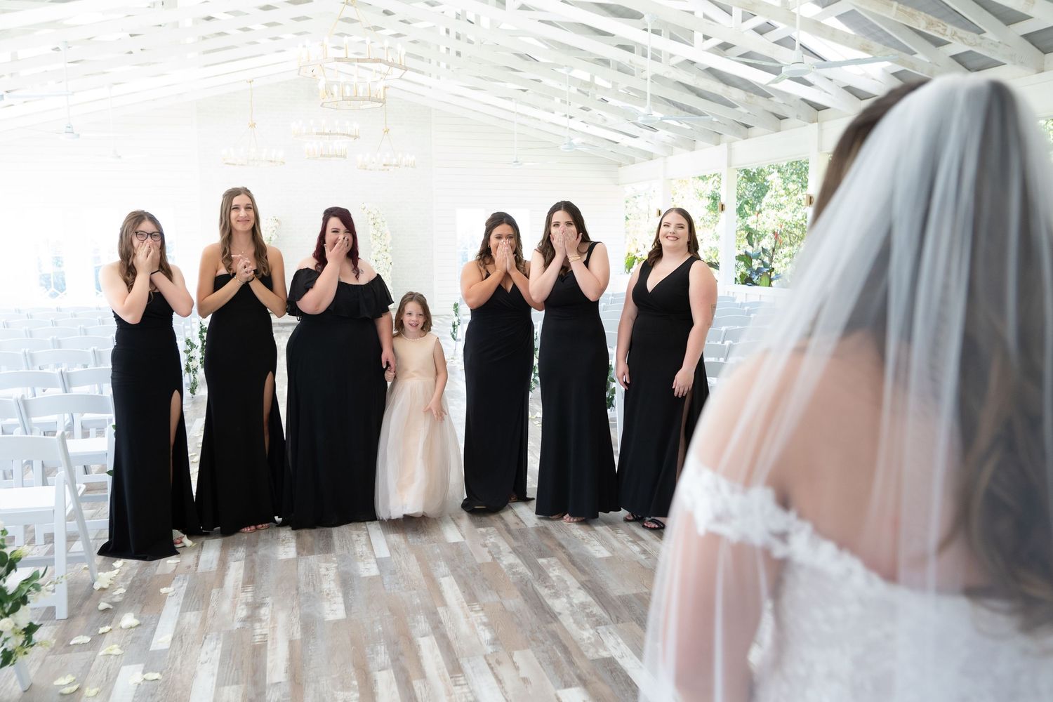 A row of bridesmaids in black dresses and one bride in white pose together for a formal wedding photo.