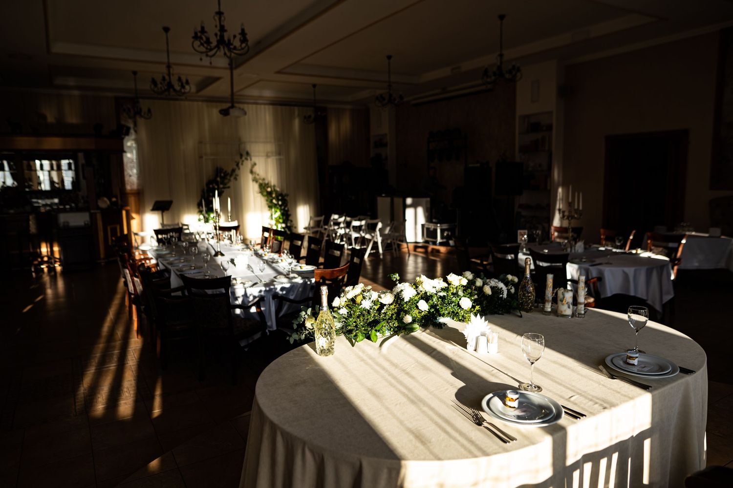 Elegant wedding reception venue with round tables and floral centerpieces illuminated by dramatic natural lighting.