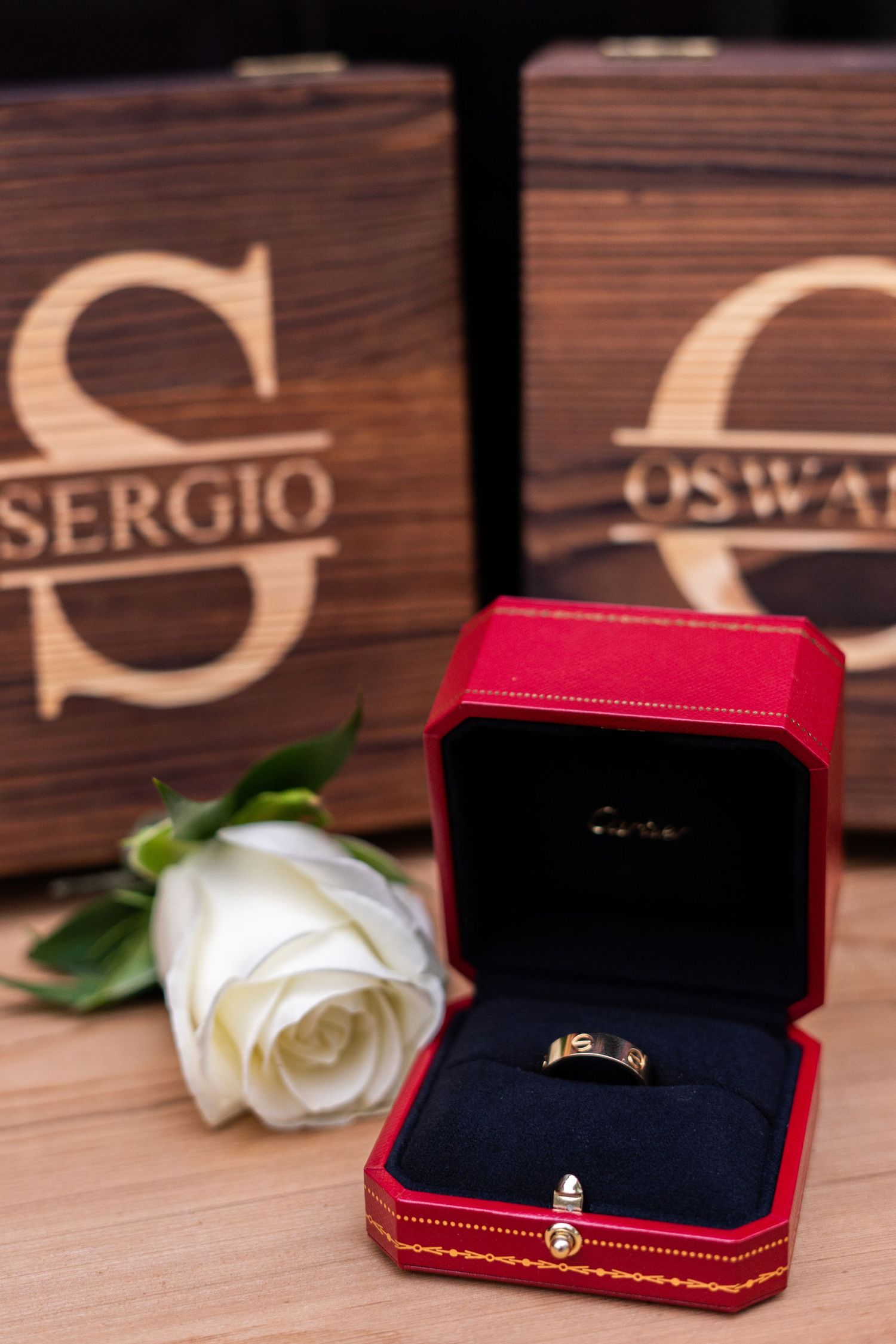 Four elegant engagement ring boxes in red and navy velvet arranged with a white rose on a wooden surface.
