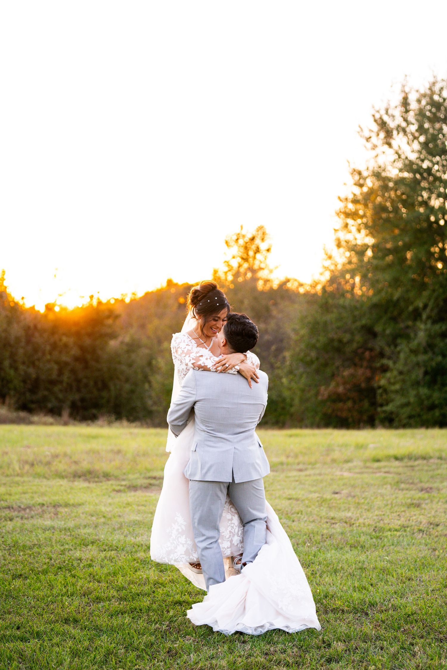 A romantic sunset photoshoot of a couple in wedding attire embracing in a grassy field.