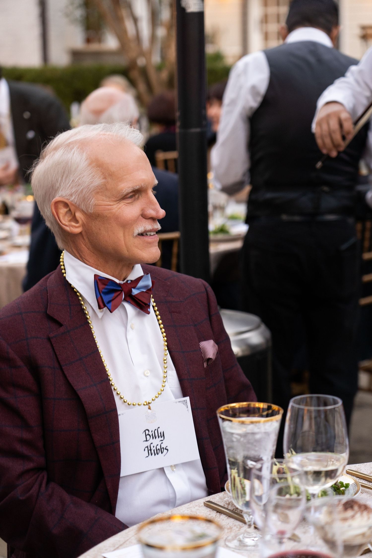 Guest wearing burgundy jacket and bowtie seated at formal dinner table.