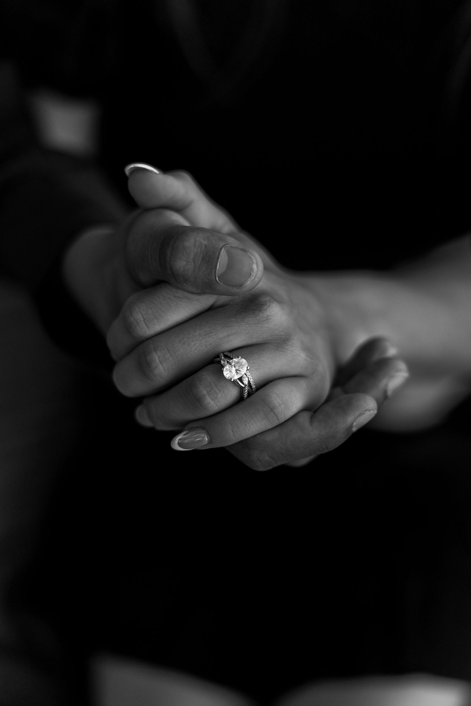 Black and white close-up of clasped hands with an engagement ring.