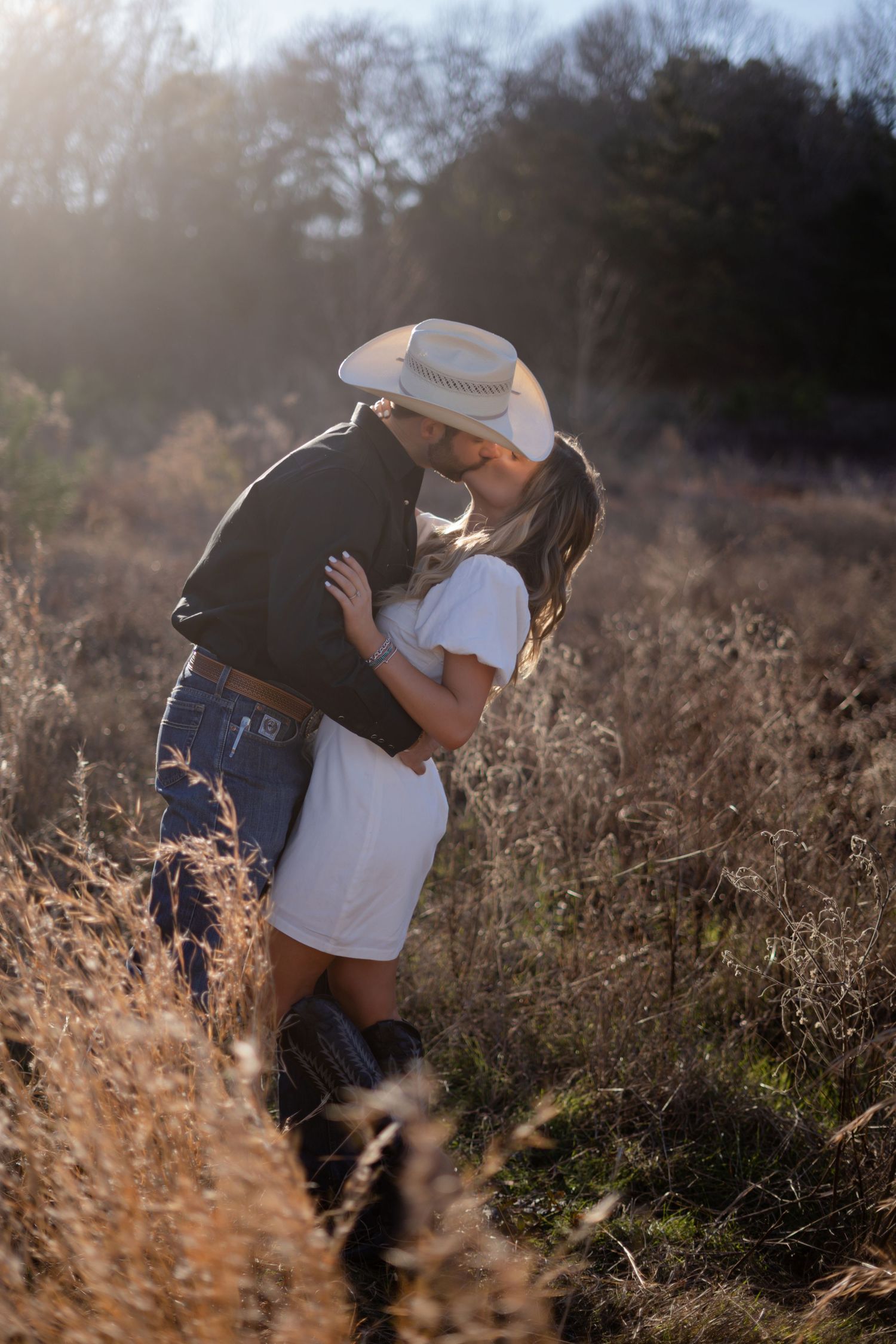Intimate couple photos captured in a sun-lit field with dried grass and natural scenery.