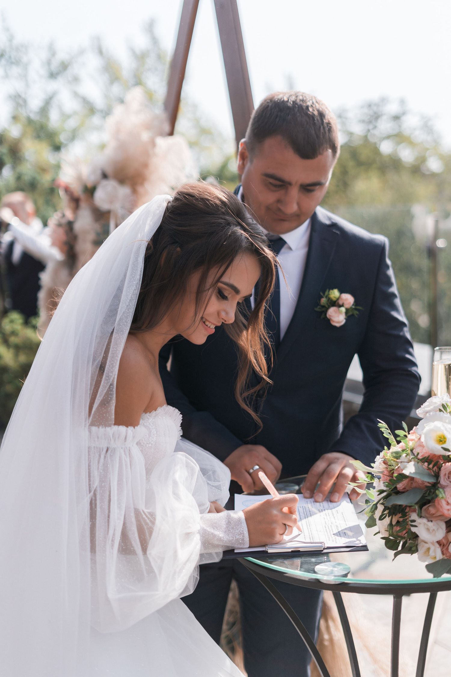 Wedding couple signing official documents at an outdoor ceremony.