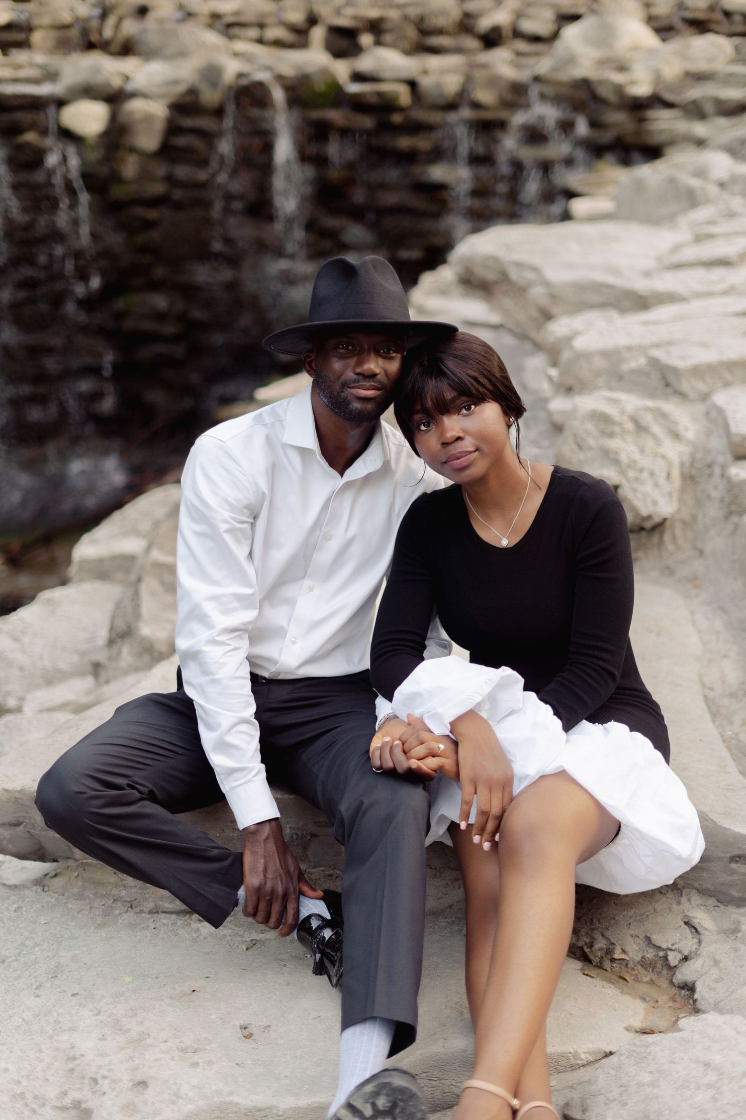 Couple in contrasting outfits posing on rocky landscape.