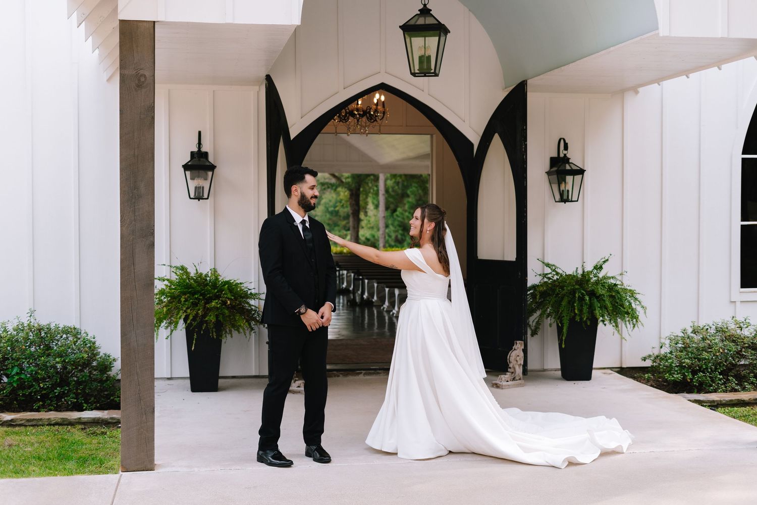 A wedding couple shares a private moment under the white arched portico of a chapel.