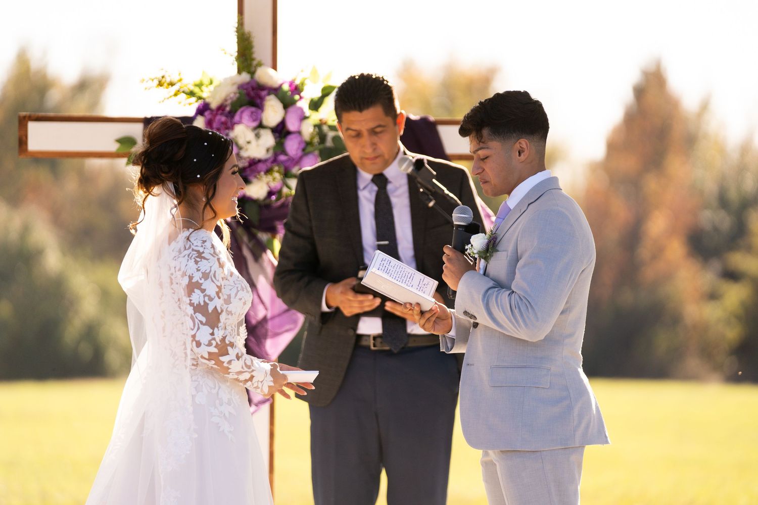 Wedding party poses outdoors in purple and gray attire during golden hour celebration.