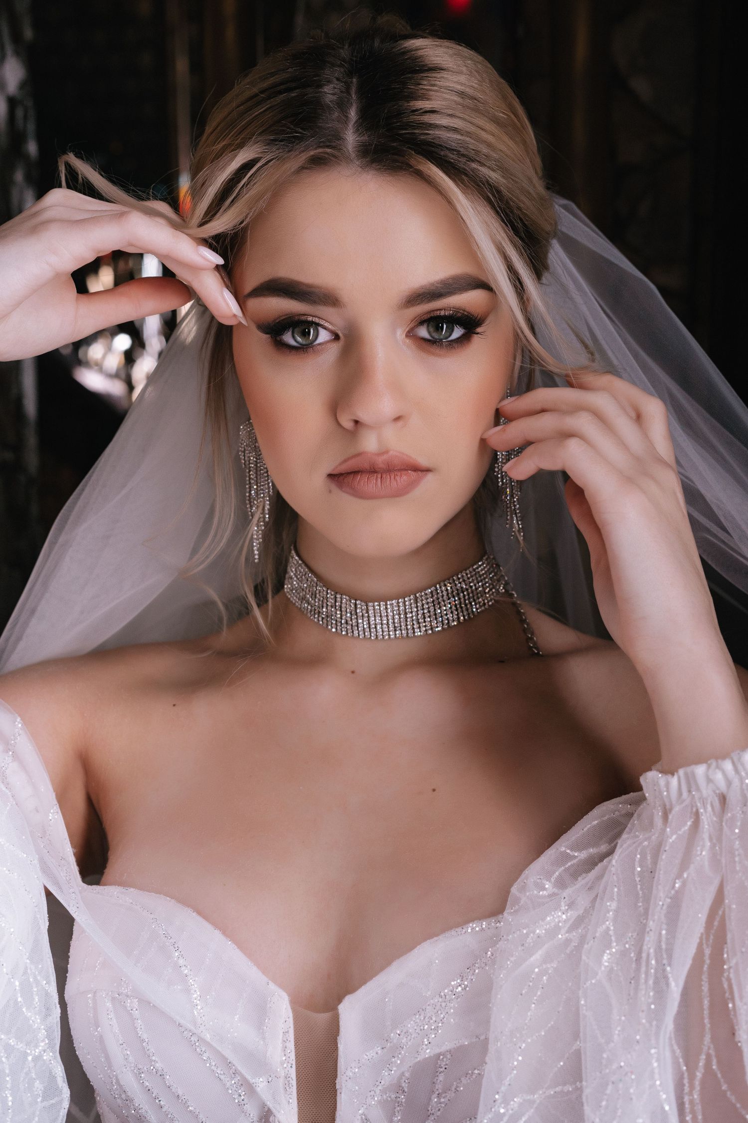 A bride in a white wedding dress and veil poses for a series of close-up portraits wearing a crystal choker necklace.
