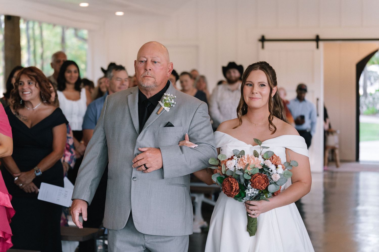Wedding ceremony guests gather in an elegant white indoor venue.
