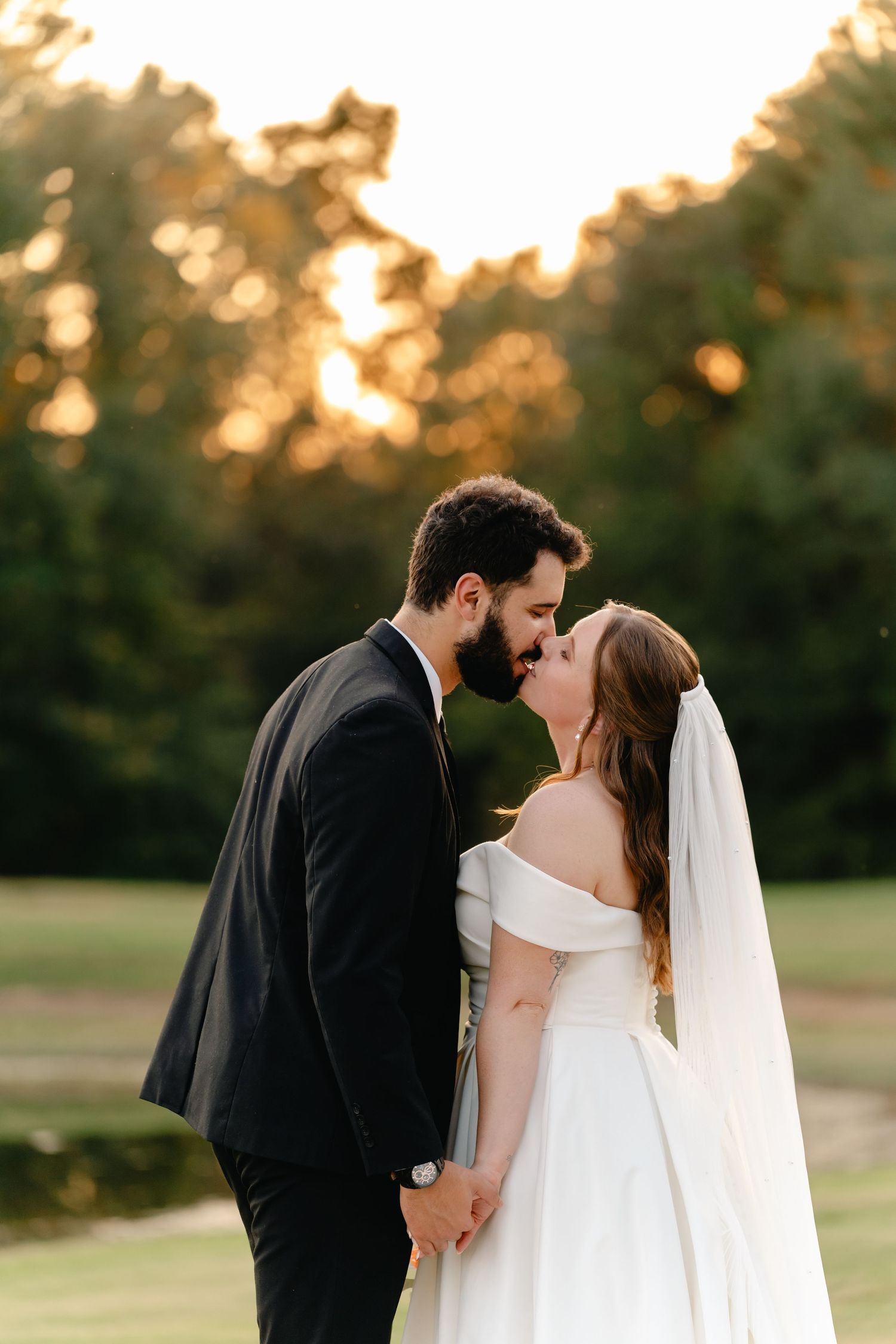 A romantic sunset wedding portrait captures newlyweds sharing an intimate moment in a golden field.