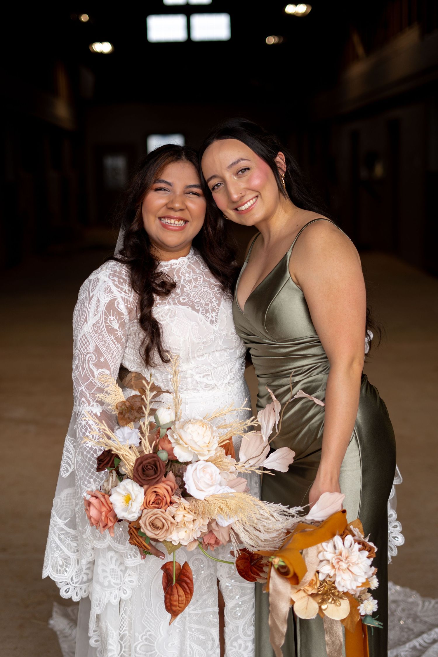 Wedding party members in white lace and sage green dresses hold autumn-colored bouquets.