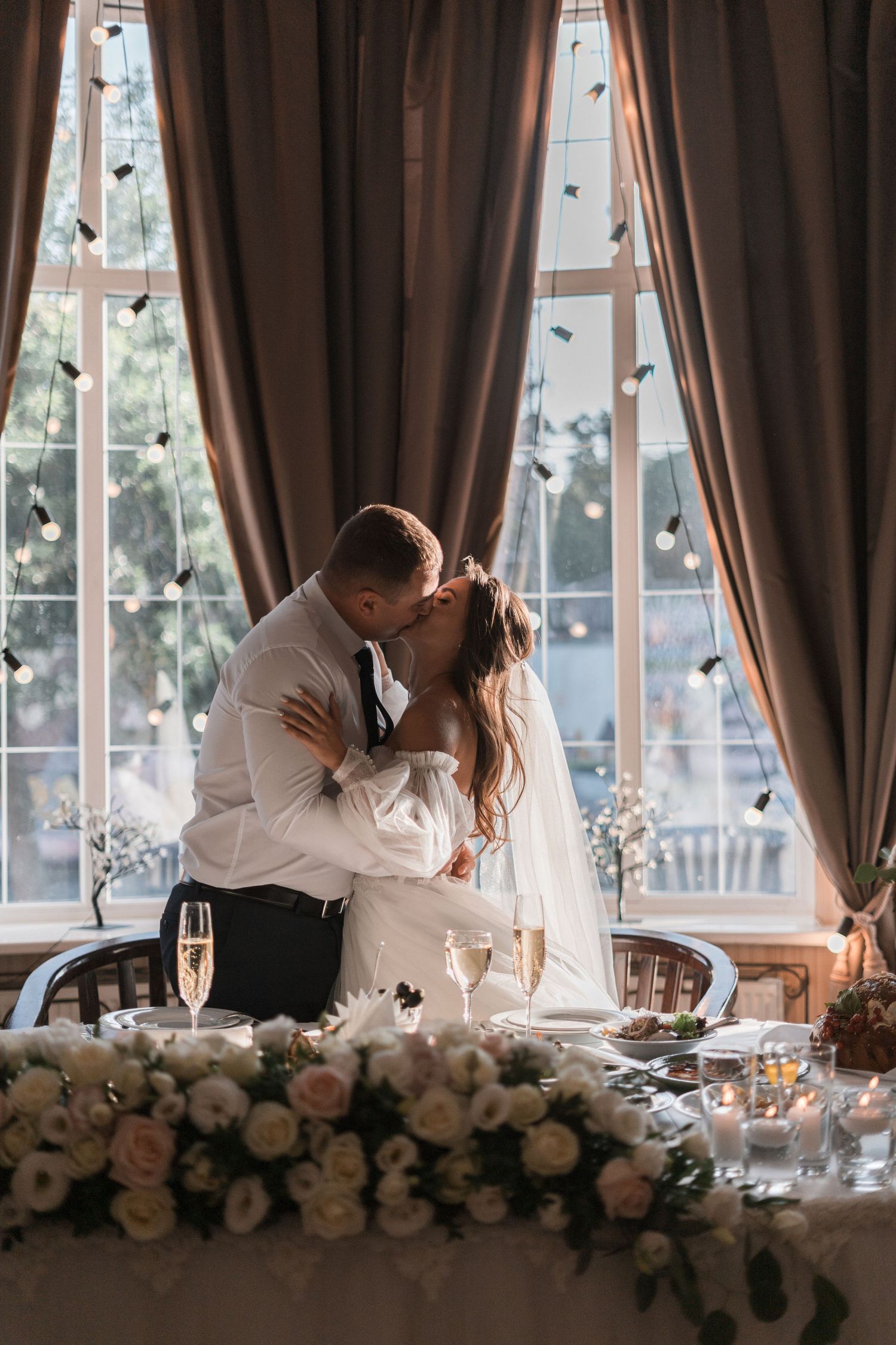 A romantic moment between newlyweds at their wedding reception with elegant floral decorations and champagne glasses.