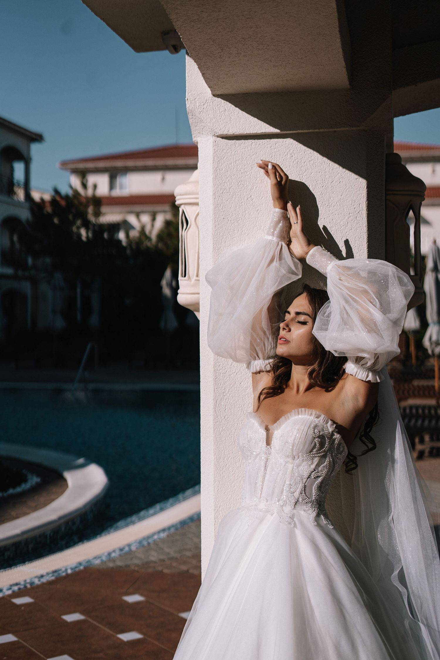 A bride in a flowing white wedding dress twirls with her veil in an outdoor setting during a photoshoot.