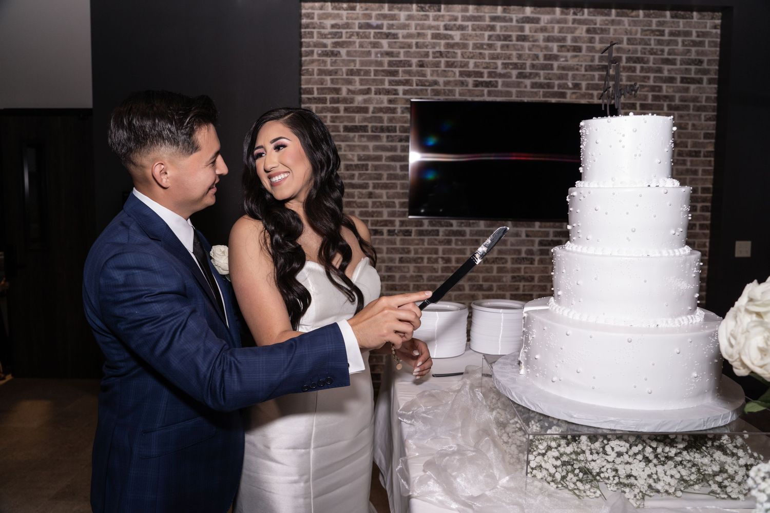 A series of wedding reception photos showing a white tiered cake being cut and shared at a brick-walled venue.