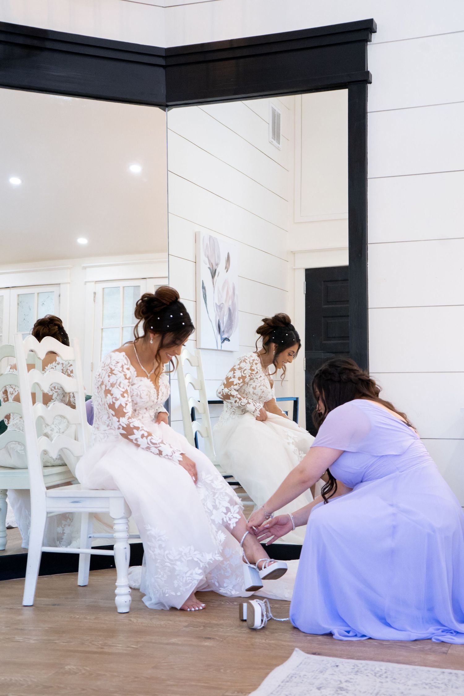 Wedding party members help arrange the bride's dress while reflected in mirrored walls.