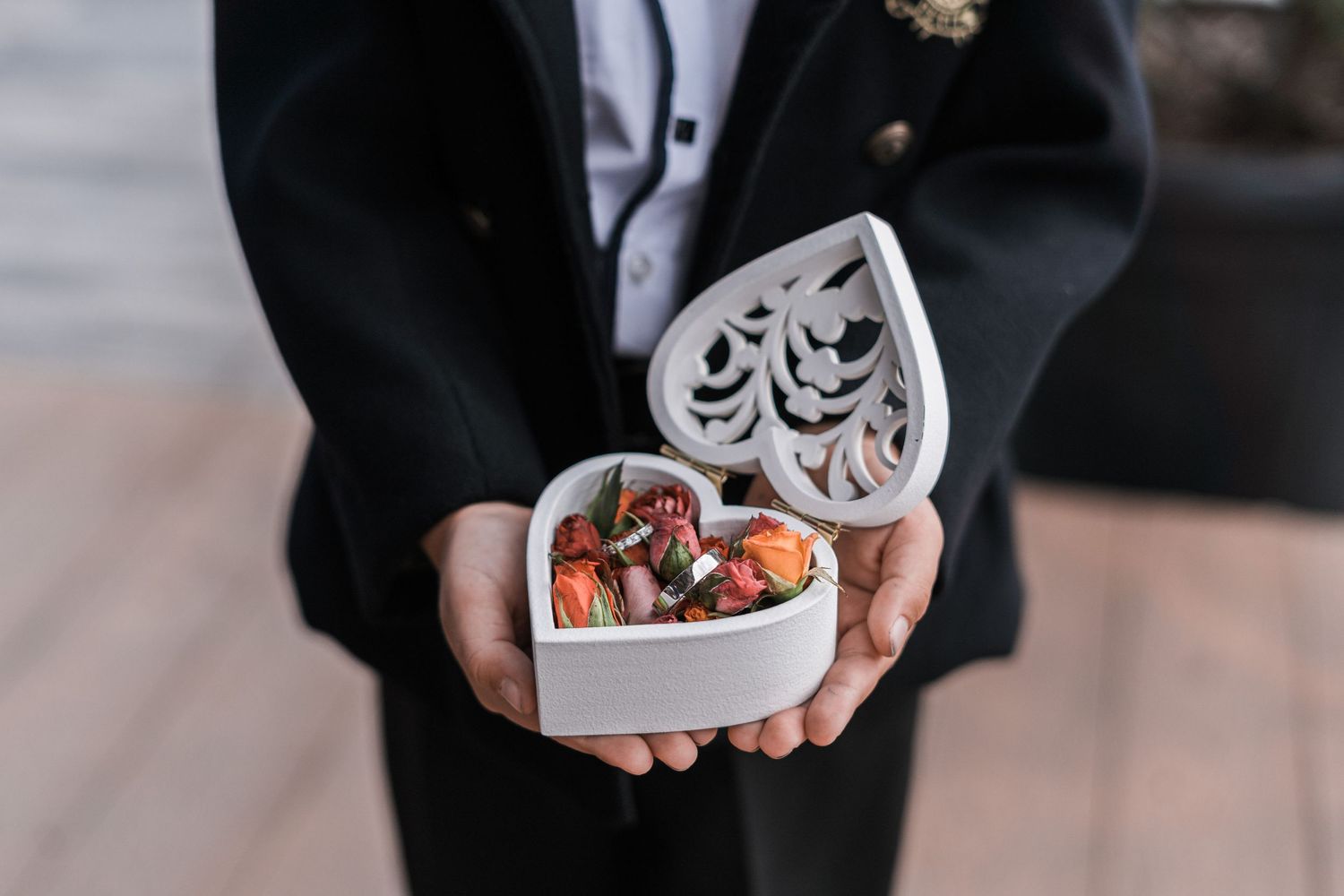 Hands in dark sleeves holding white gift boxes and jewelry against a neutral background.