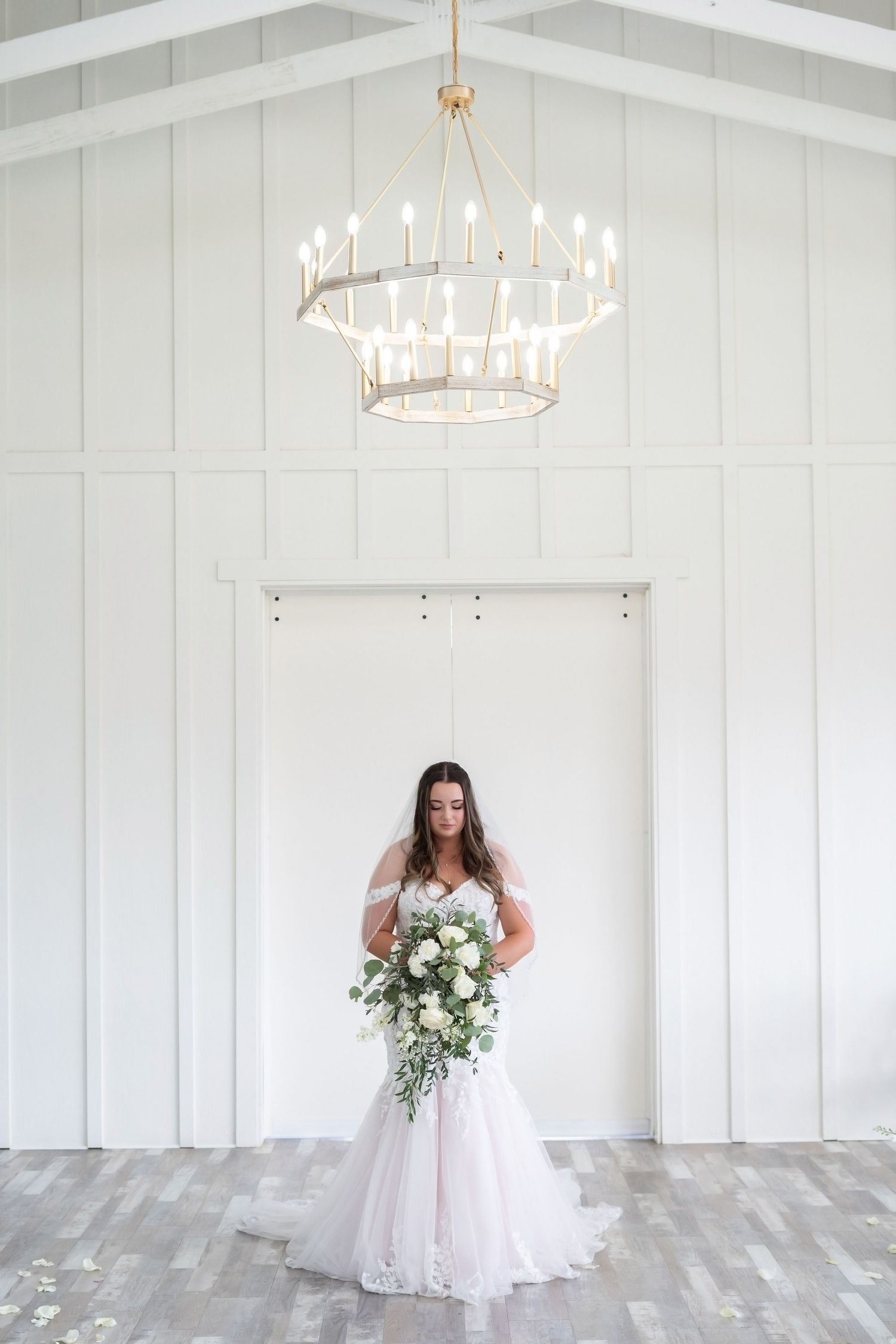 A white wedding venue interior with elegant chandelier and gray flooring showcases a beautiful bridal portrait.