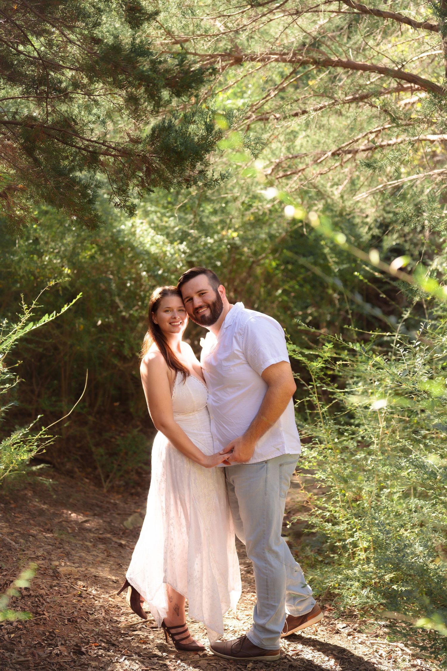 Casual engagement session in wooded setting with couple in coordinating white outfits.