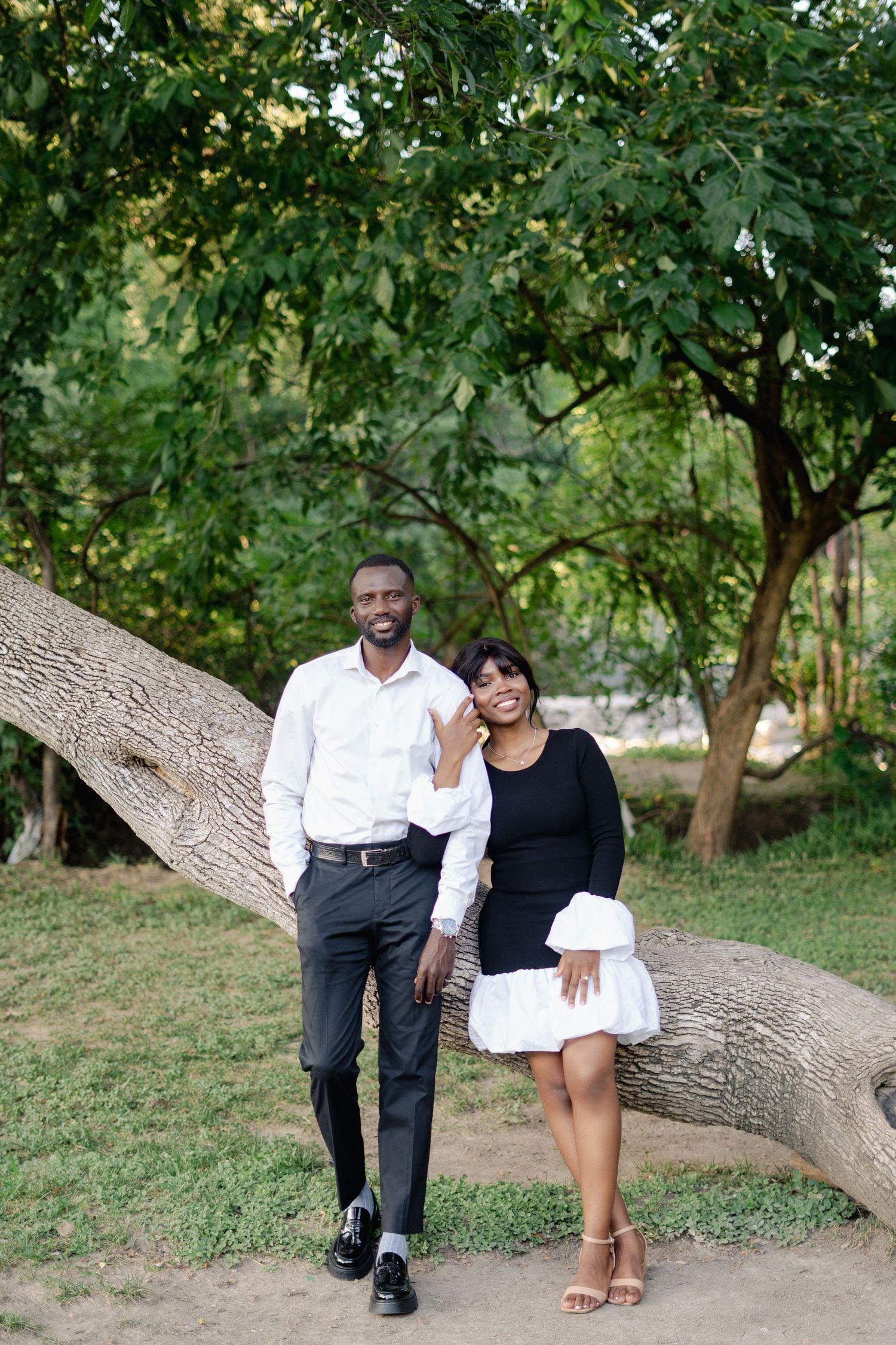 Couple relaxing on fallen tree trunk in park setting.