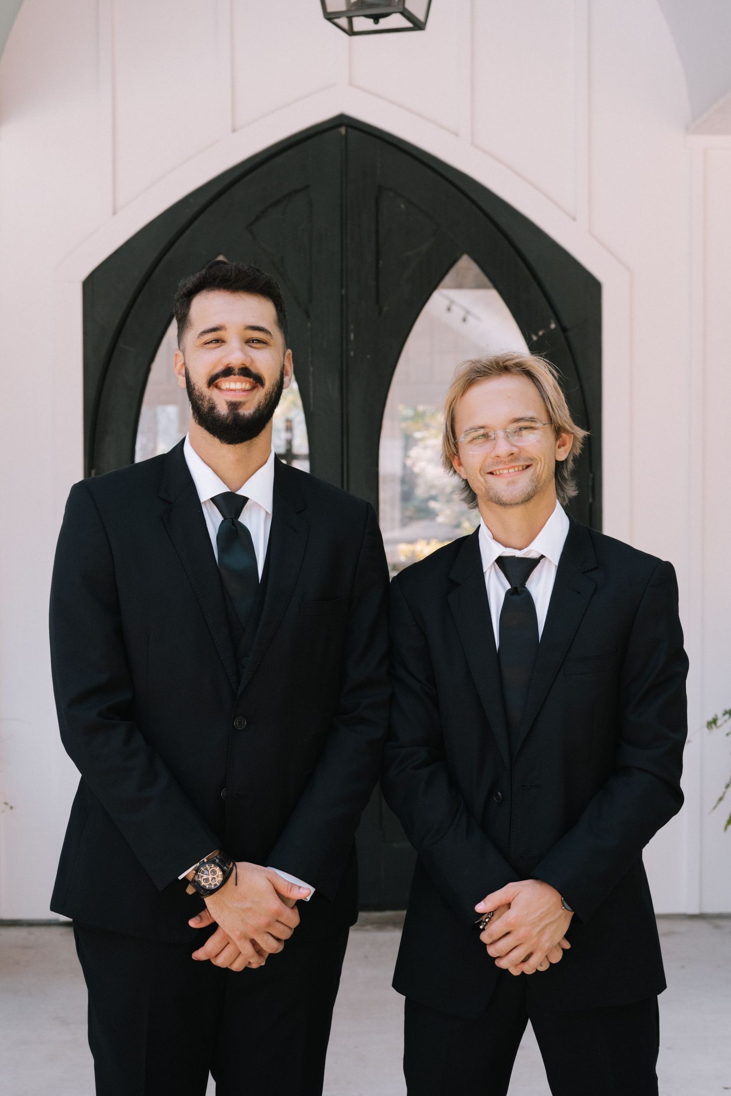 Wedding party members in black suits standing together outside chapel entrance.