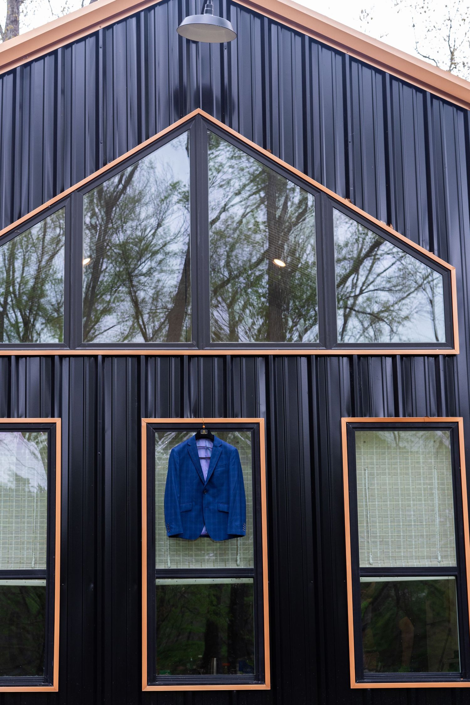 Modern building exterior with black metal siding, orange trim accents, and large windows displaying blue suit jackets.