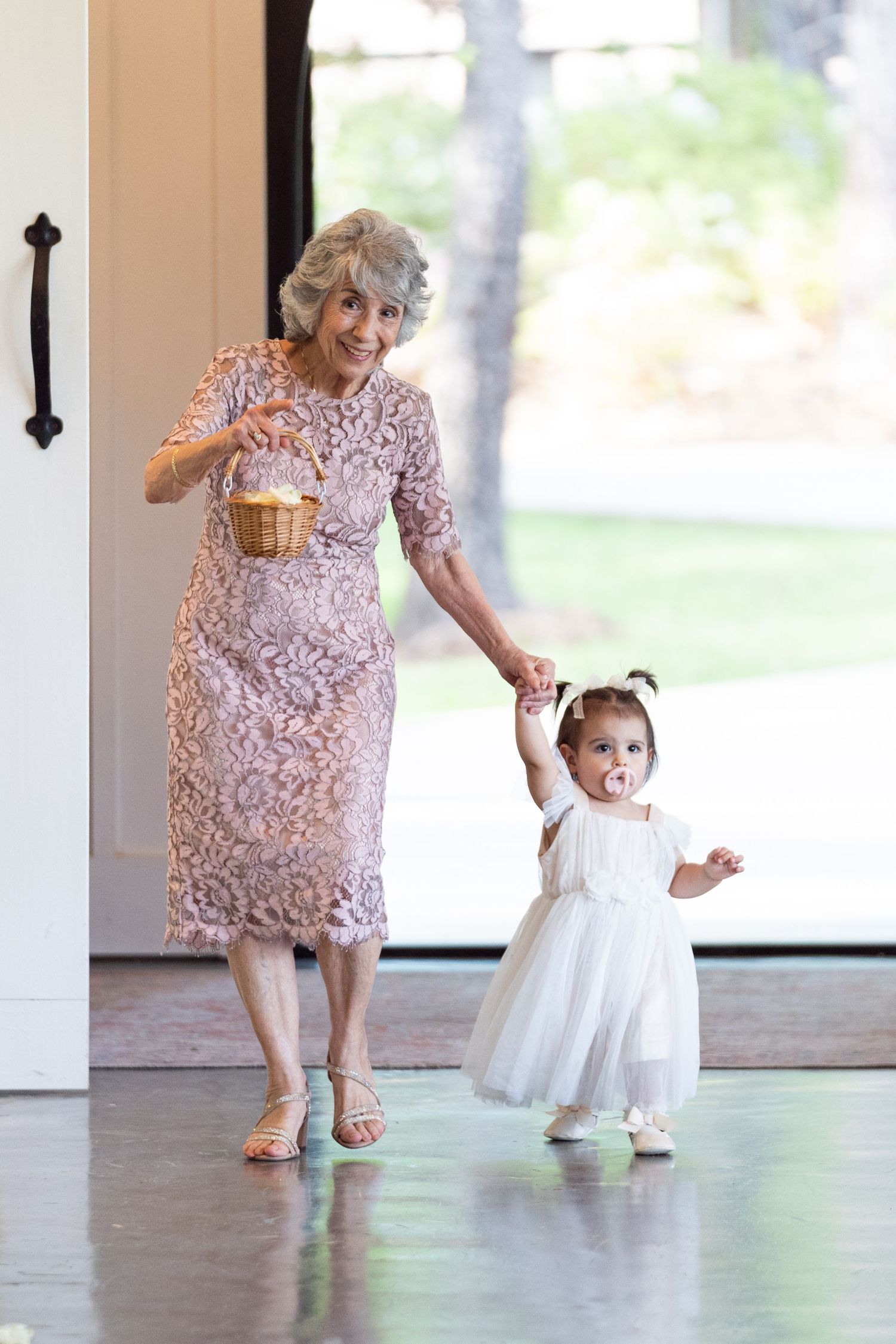 A grandmother and young child dance together in a sunlit room, wearing pink lace and white dresses.