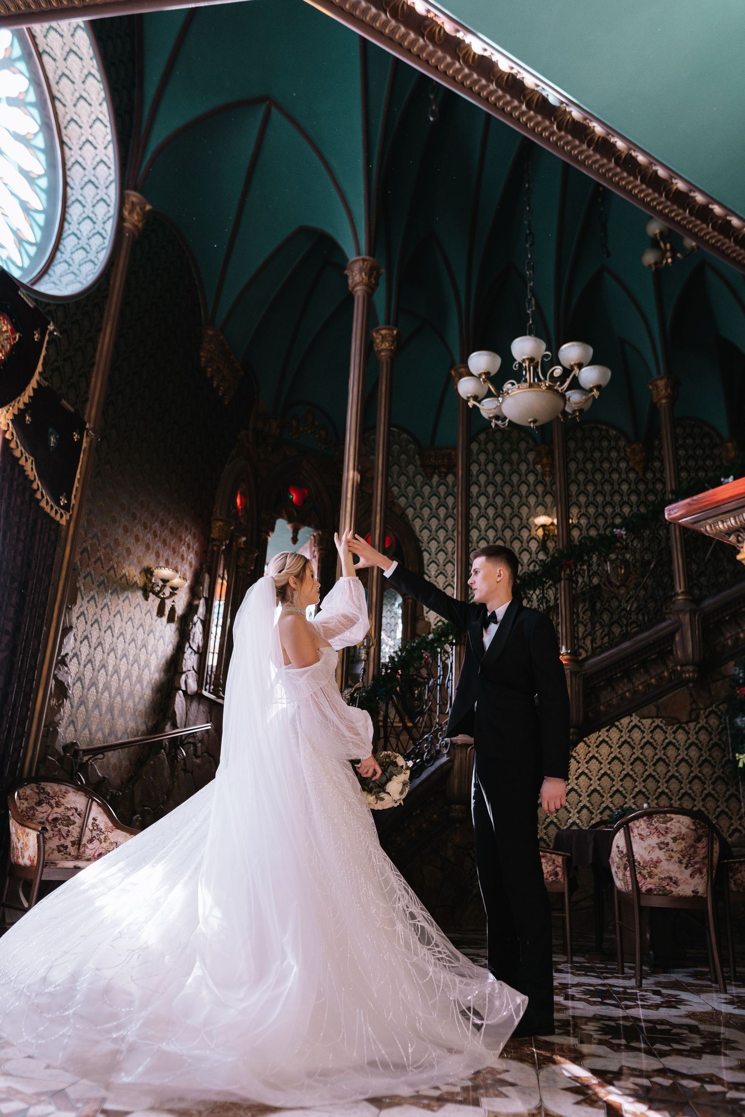 Bride and groom dance together in an ornate ballroom with elegant vintage decor and chandeliers.