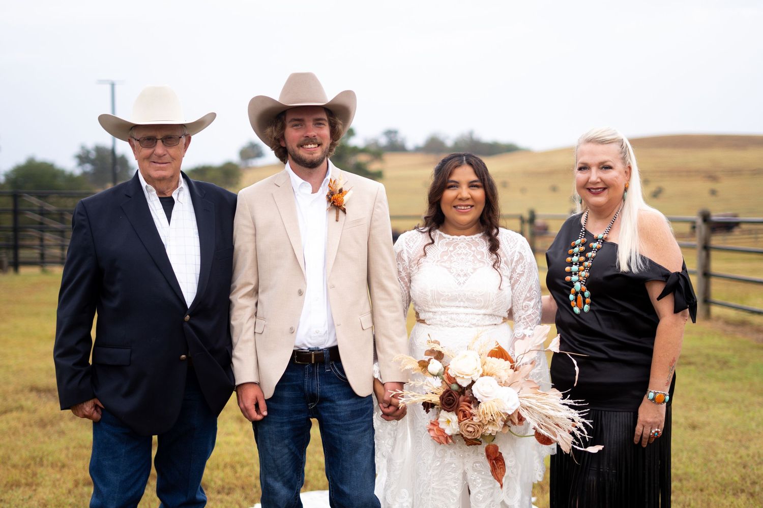 Wedding group wearing cowboy hats and formal attire stands in grassy field.