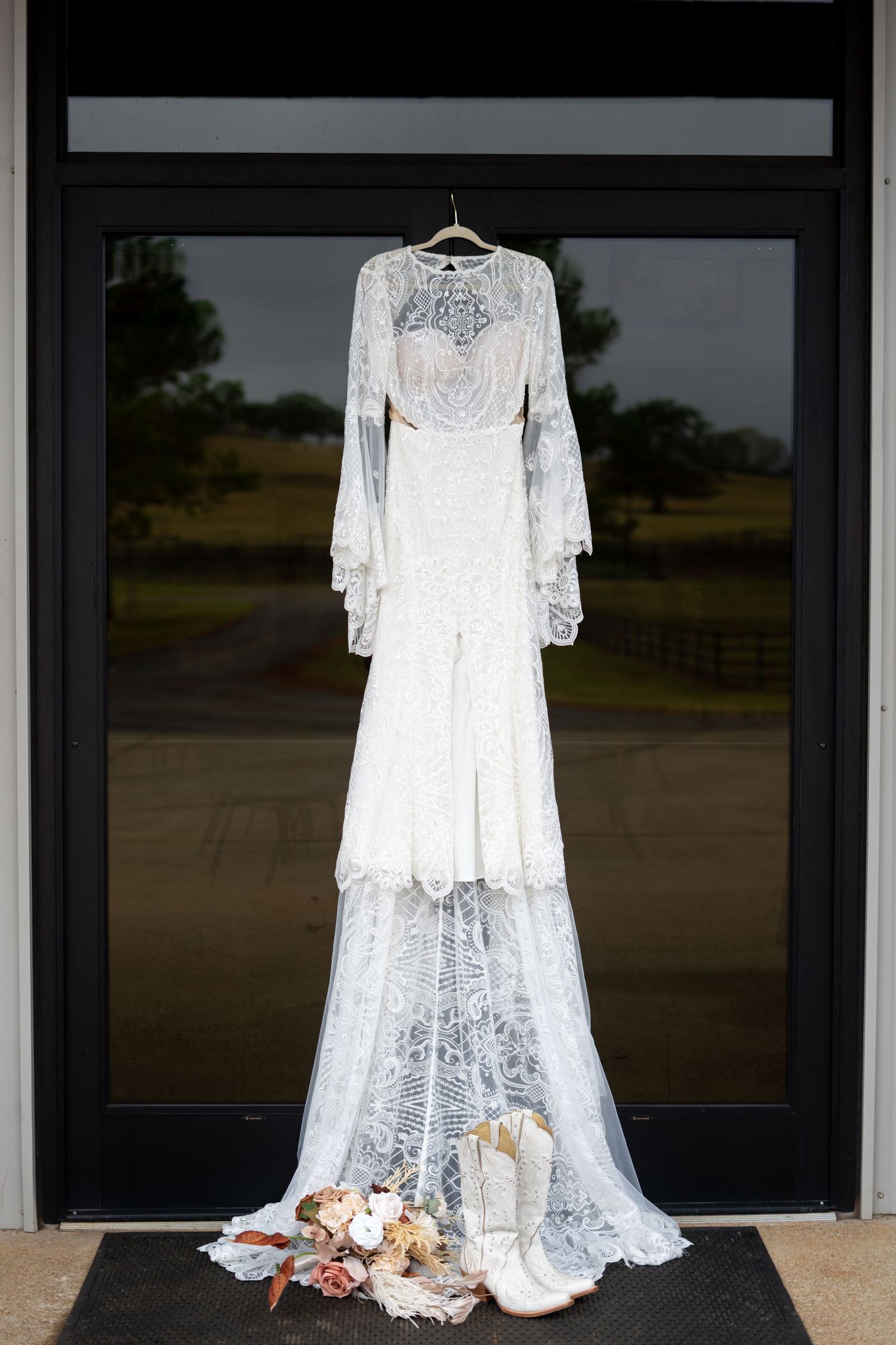 Elegant white lace wedding dress displayed with floral bouquet against dark background.