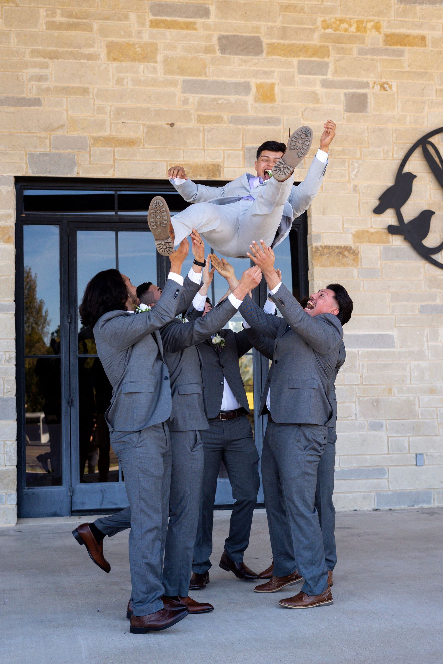 Groomsmen in gray suits performing a fun boot-drinking celebration ritual outdoors.
