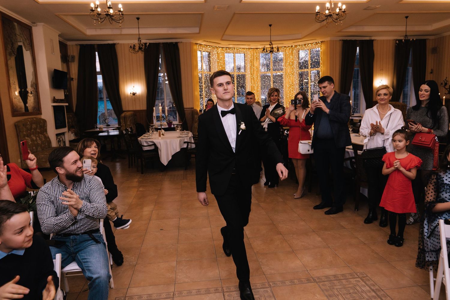 People dancing and celebrating at an elegant indoor venue with chandeliers and hardwood floors.