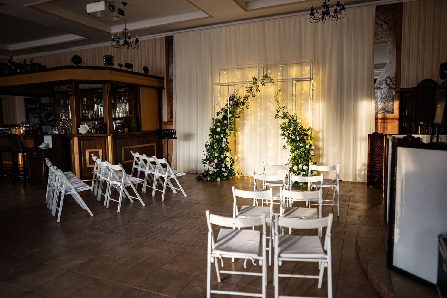 Elegant white wedding reception venue with draped fabric walls and floral arrangements illuminated by warm lighting.