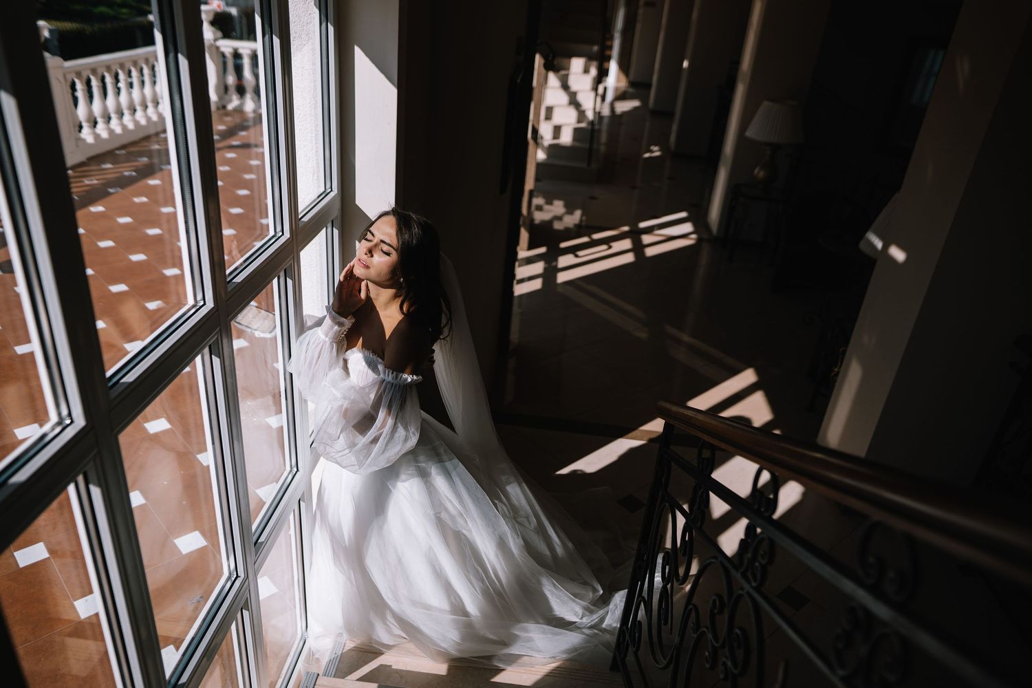 A bride in a white wedding dress stands by a window, creating a silhouetted profile against natural light.