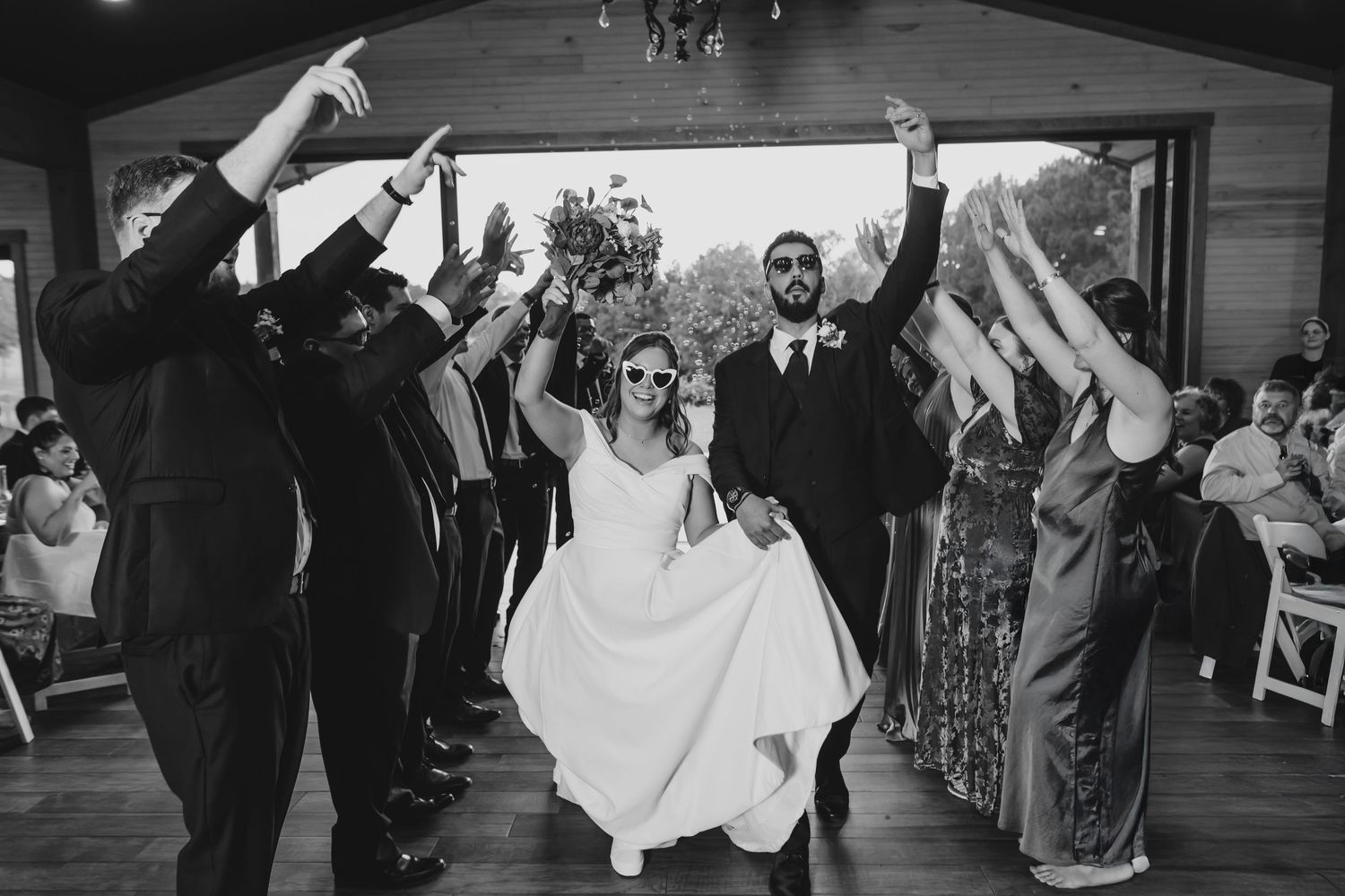 Wedding reception guests dance and celebrate on a dimly lit dance floor.