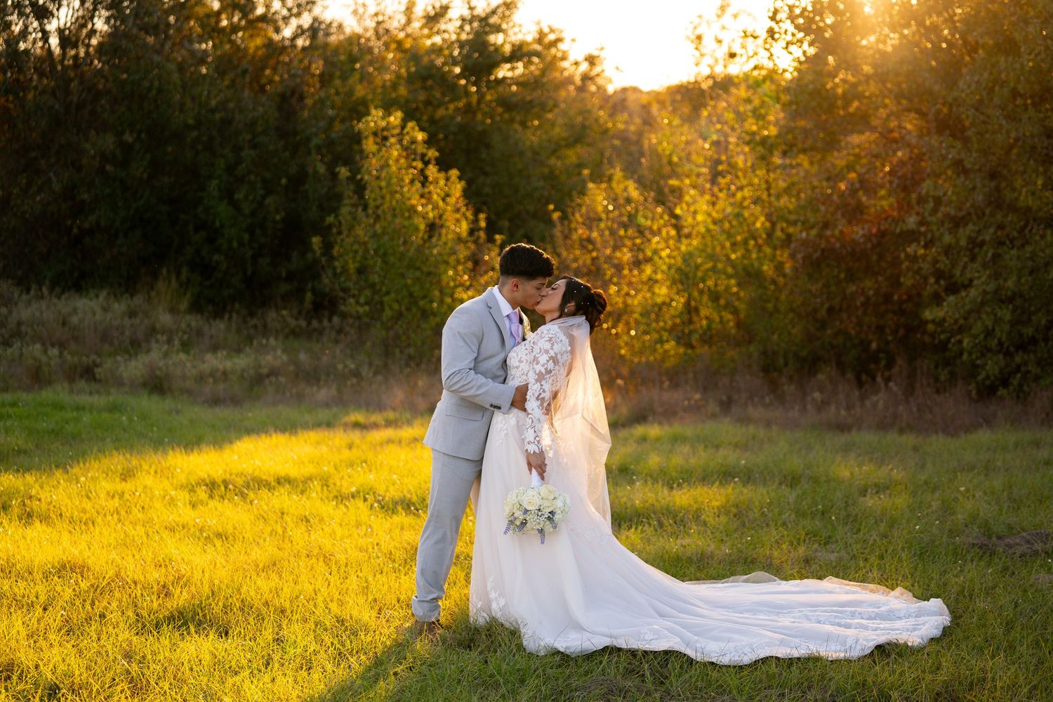 Wedding couple embracing in golden sunset light on grassy field.