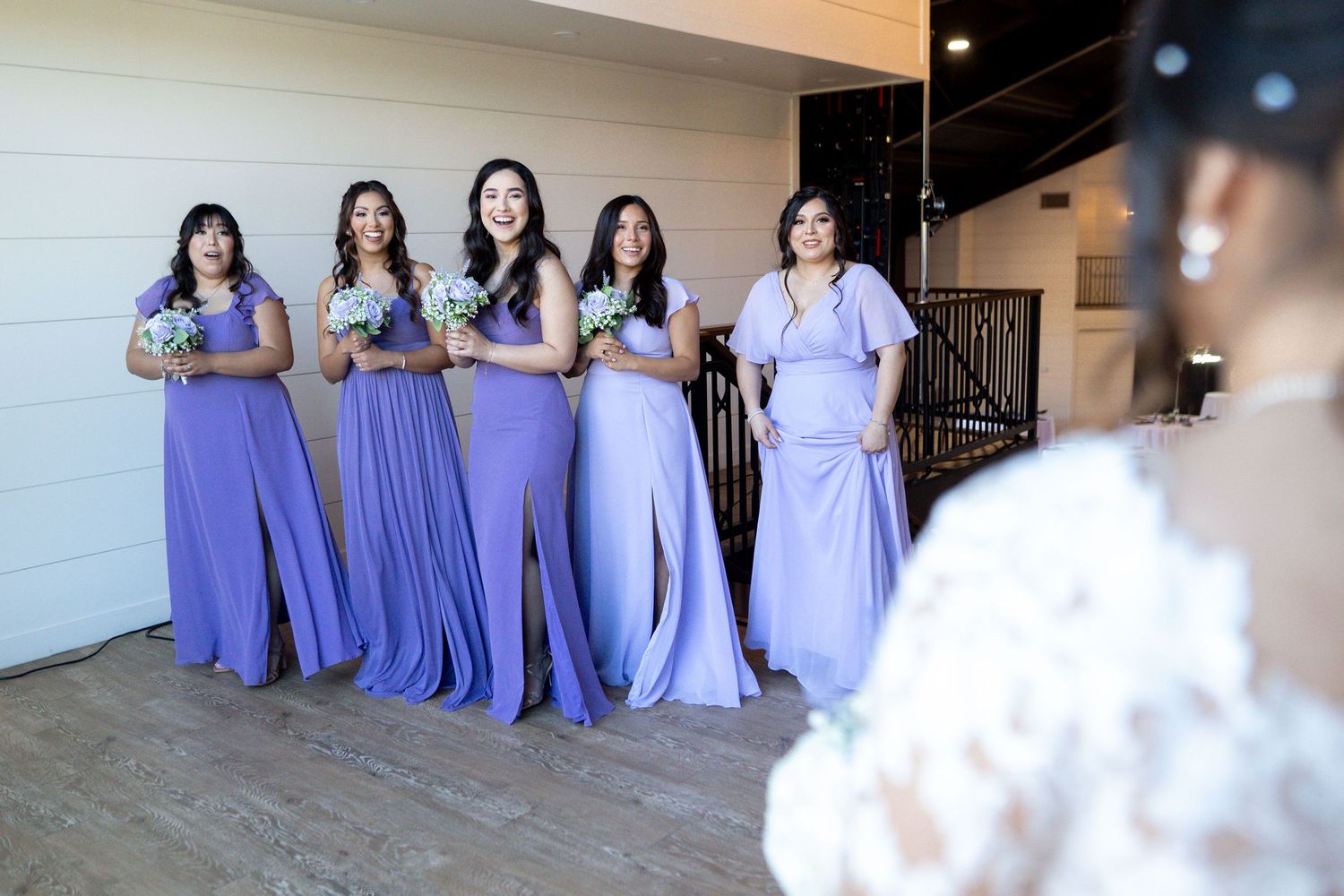 Bridesmaids wearing flowing lavender dresses seated together indoors.