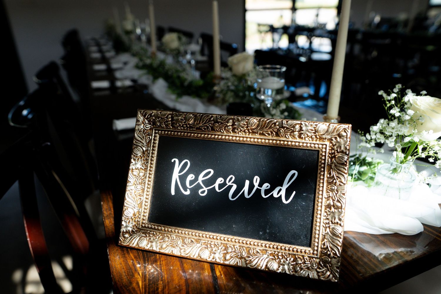 Elegant gold-framed chalkboard sign with 'Reserved' text sits on a rustic wooden surface at an event venue.