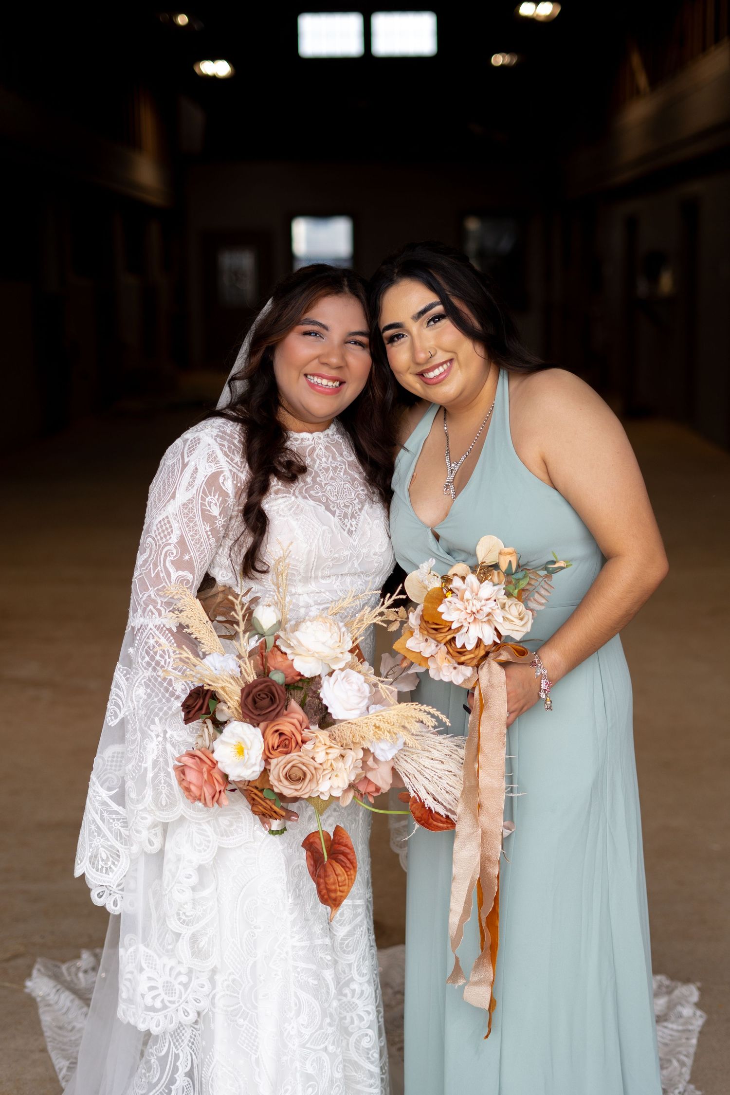 A bride and bridesmaid share a joyful moment while holding a floral bouquet.