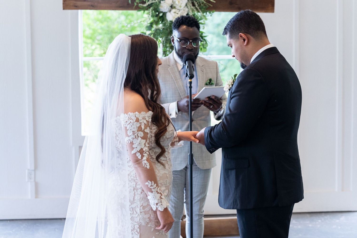 A couple exchanges rings during an intimate indoor wedding ceremony with an officiant present.