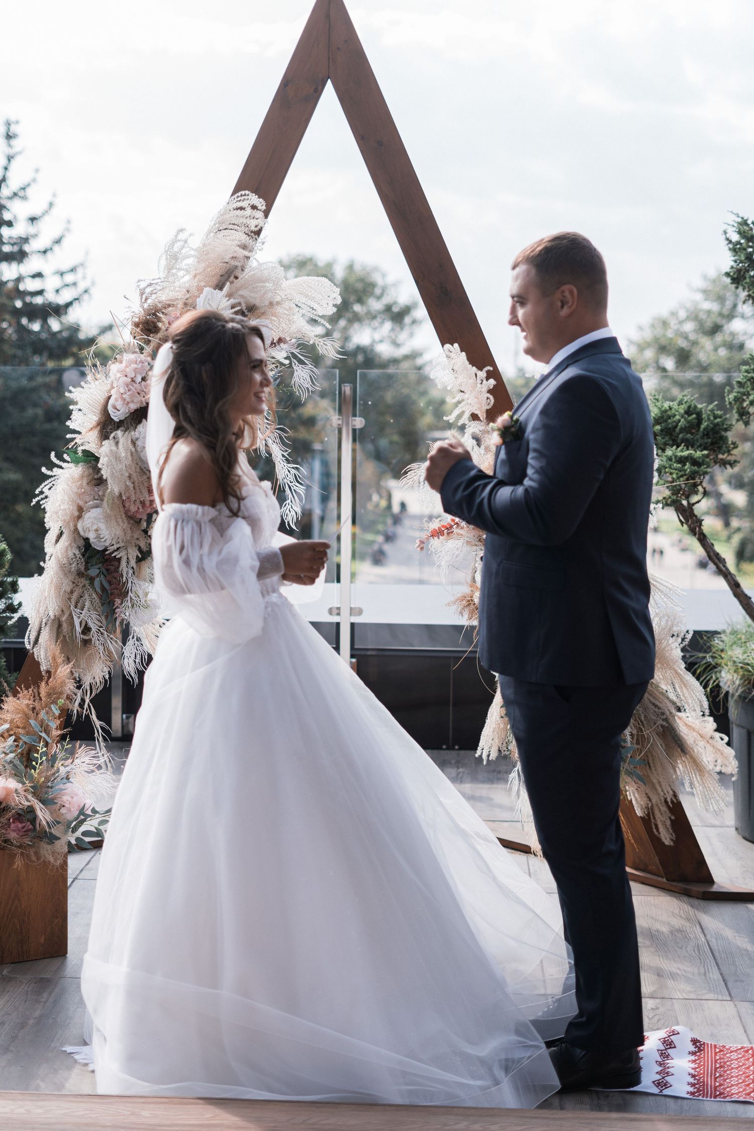 A couple in wedding attire dances together under a wooden A-frame structure in a romantic outdoor setting.