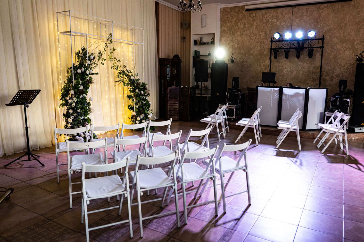 Wedding ceremony setup with white folding chairs and floral arch in an industrial-style venue with mood lighting.