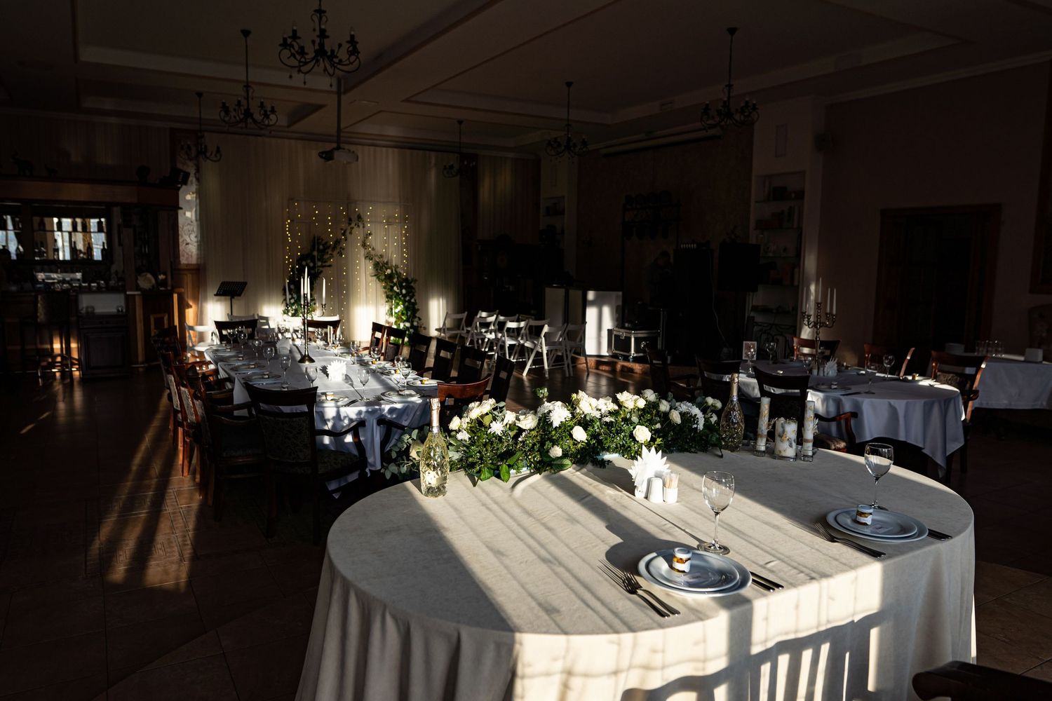 Elegant wedding reception venue with round tables, chandeliers, and white floral centerpieces in a grand ballroom.