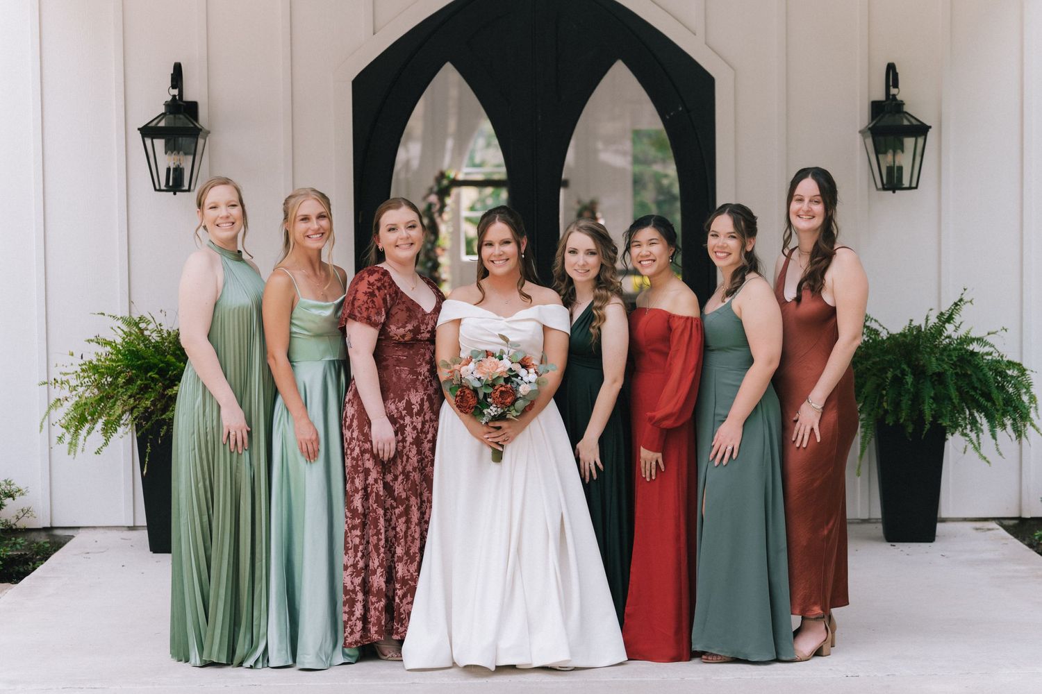 A group in coordinating sage green and burgundy dresses stands together for a formal event photo.