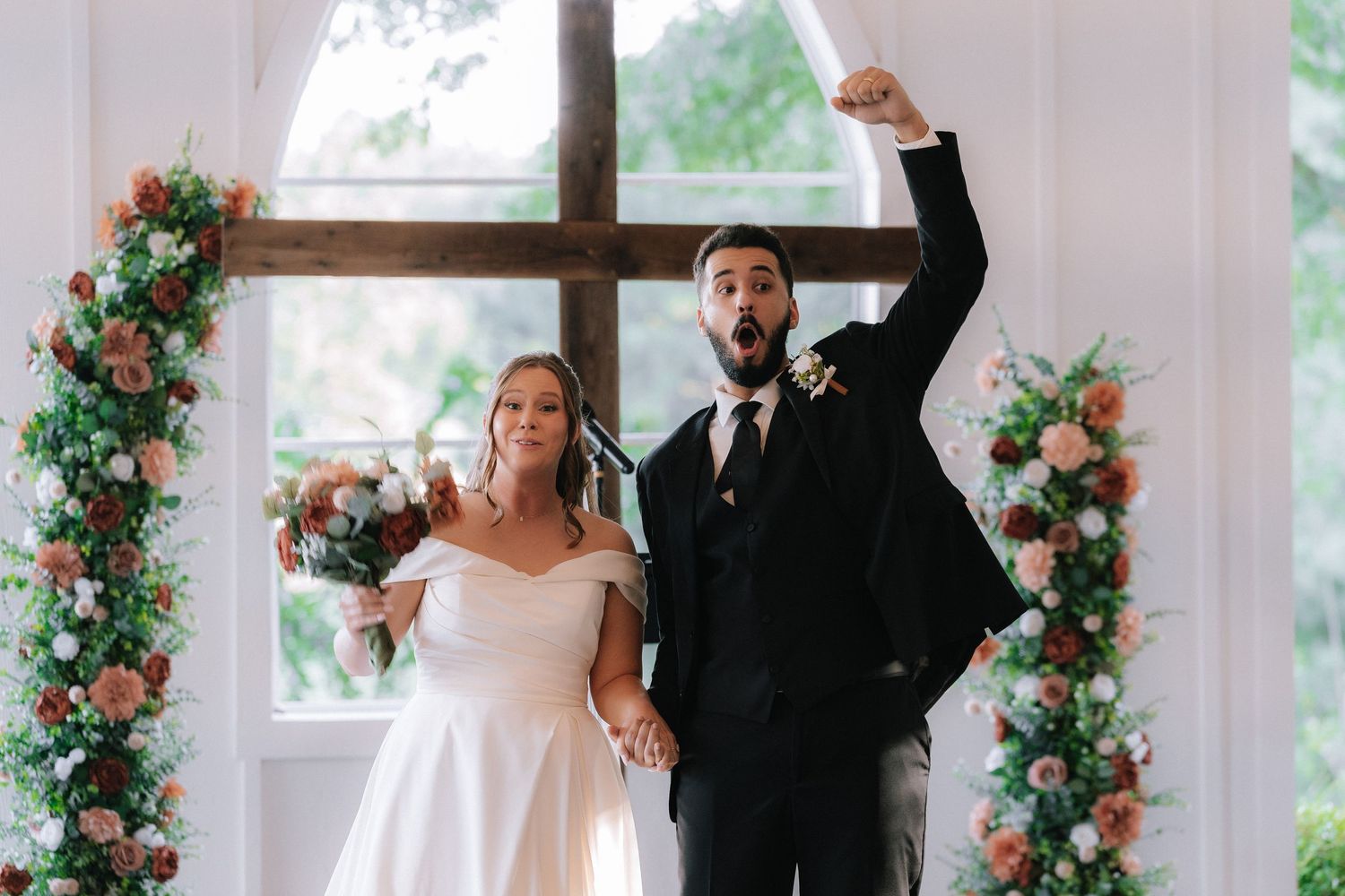Joyful wedding celebration with floral arch decorations in white indoor space.
